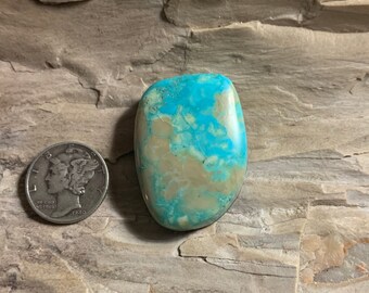 May include: A turquoise cabochon with a blue-green and brown color pattern. The stone is oval shaped and has a smooth, polished surface.