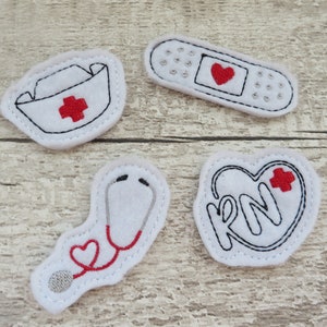 May include: Four white felt patches with embroidered designs related to nursing. The patches include a nurse's cap with a red cross, a stethoscope with a red heart, a bandage with a red heart, and a heart with the letters "RN" and a red cross.