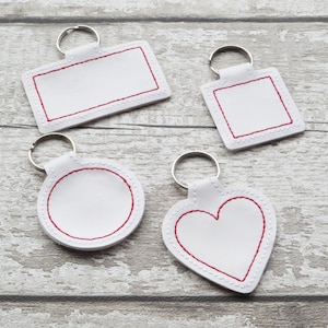 May include: Four white leather keychains with red stitching. The keychains are shaped like a rectangle, circle, heart, and square.