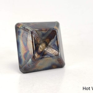 May include: A square-shaped metal object with a textured surface. The object has a metallic blue, brown, and gold color. The object is labeled "Hot Waxed".