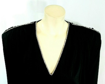 May include: A black long-sleeved top featuring a deep V-neckline and shoulder seams accented with a single row of clear, sparkling rhinestones. The garment is displayed on a mannequin, highlighting the dark fabric and the reflective crystal trim.