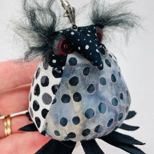 May include: A black and white polka dot fabric owl keychain with a silver chain and black fur accents.