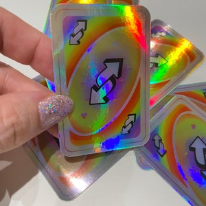 May include: Holographic reverse Uno cards with a rainbow swirl design. The cards feature a silver border and the reverse symbol with arrows. The cards are scattered on a white surface.