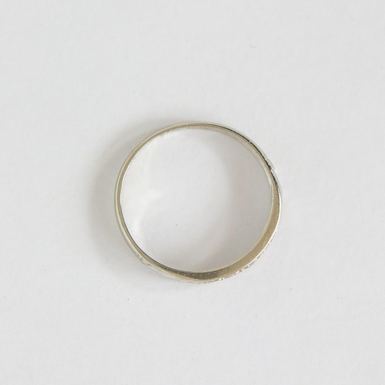 May include: A silver ring with a simple band design. The ring is circular and appears to be made of a shiny metal. The ring is set against a white background.