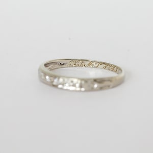 May include: A silver-colored ring with etched text inside. The ring has a textured surface and a simple band design. The text inside the ring reads "A. Tata No. F 3233".