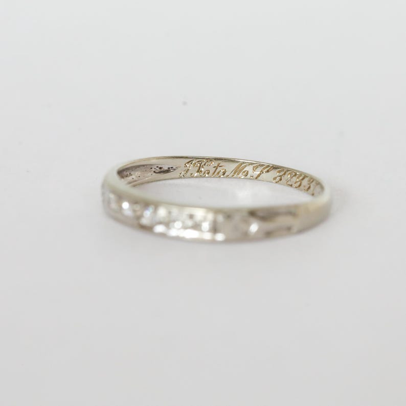May include: A silver-colored ring with etched text inside. The ring has a textured surface and a simple band design. The text inside the ring reads "A. Tata No. F 3233".