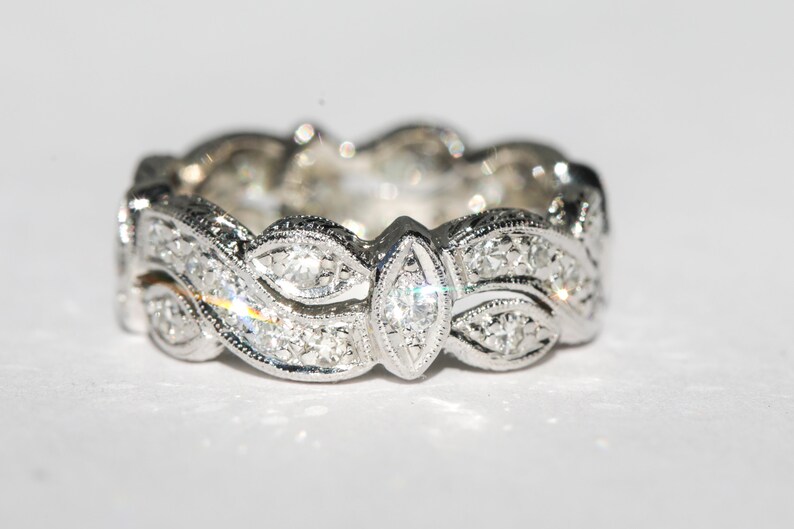 Pu&ograve; includere: Un anello a fascia d'argento con un design delicato e intricato che presenta una fila di piccoli diamanti e un diamante pi&ugrave; grande di forma a marquise al centro.