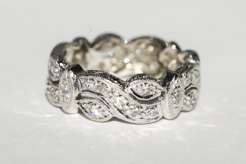 Pu&ograve; includere: Un anello a fascia d'argento con un design delicato e intricato che presenta una serie di piccoli diamanti incastonati in un motivo ondulato.