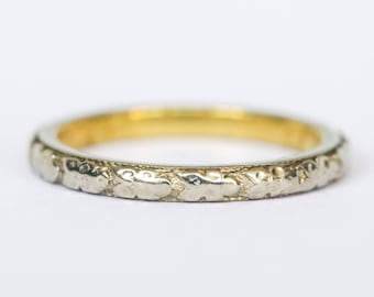 May include: A delicate gold and silver wedding band with a floral design.