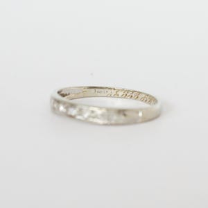 May include: A white gold ring with small, clear stones set along the band. The ring has engraved text on the inside. The ring is set against a white background.