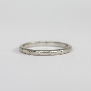 May include: A thin, silver-colored metal ring featuring a continuous, repeating engraved pattern along its entire outer band. The surface of the ring has a polished, reflective finish, showcasing a series of small, interconnected, leaf-like shapes.
