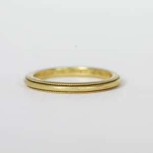 May include: A gold-colored ring with a beaded design on the edges. The ring has a simple, elegant style, suitable for everyday wear. The ring is approximately 0.25 inches wide.