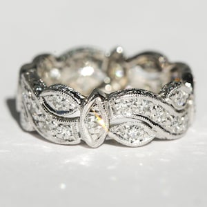 Pu&ograve; includere: Un anello a fascia d'argento con un delicato design a onde, caratterizzato da una fila di piccoli diamanti e un diamante pi&ugrave; grande di forma a marquise al centro.