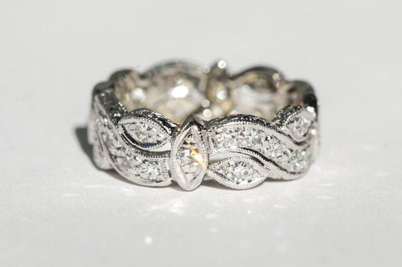 Pu&ograve; includere: Un anello a fascia d'argento con un delicato design a onde, caratterizzato da una fila di piccoli diamanti e un diamante pi&ugrave; grande di forma a marquise al centro.