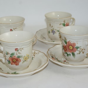 May include: Set of four floral teacups and saucers. The cups and saucers are white with a floral pattern in shades of red, orange, yellow, and green. The cups have a gold rim.