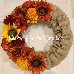 May include: A fall-themed wreath with sunflowers, mums, and other flowers in shades of yellow, orange, and red. The wreath has a burlap base and the text "Wickedly Perfect Creations".