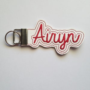 May include: White leather keychain with a red embroidered name "Ailyn" in a cursive font.