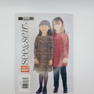 May include: A sewing pattern for two children's dresses. The pattern is called "see & sew" and is labelled "YES! It's easy." The pattern includes a leopard print dress and a solid red dress.