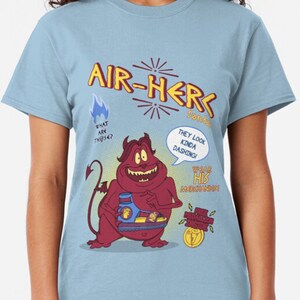 May include: Pale blue t-shirt with a cartoon graphic of a red devil character and the words "AIR-HER" in yellow. The design includes speech bubbles with the phrases "WHAT ARE THESE?" and "THEY LOOK KINDA DASHING!"