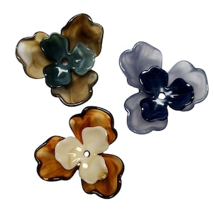 May include: Three plastic flower embellishments in different colours. The first flower is brown and beige with a green centre. The second flower is light blue and grey with a dark blue centre. The third flower is brown and beige with a white centre.