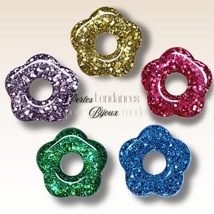 May include: Five flower-shaped beads with a glittery finish in various colours: purple, gold, red, green, and blue. Each bead has a circular hole in the centre. The text "Perles tendances pour Bijoux mode" is visible.