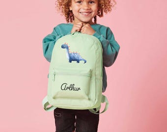 May include: A light green backpack with a blue dinosaur graphic and the name "Arthur" embroidered on the front.