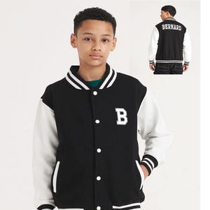 May include: A black and white varsity jacket featuring the letter "B" on the chest. The jacket has white sleeves, a black body, and white stripes on the cuffs and collar. The back of the jacket displays the name "Bernard" in white.