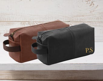 May include: Two leather wash bags. One is brown with a brown handle, and the other is black with a black handle. The black bag has gold-coloured initials "P.S." on the front. Both bags have a zip closure.