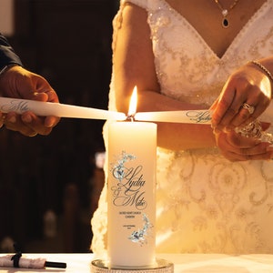 May include: A white unity candle with the names "Lydia & Mike" and the text "Sacred Heart Church Coventry" printed on it. Two people are lighting the unity candle with white taper candles.