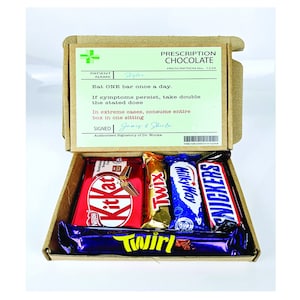 以下が含まれることがあります： 「Prescription Chocolate」と「Eat ONE bar once a day.」と書かれた処方箋ラベルが付いた茶色の段ボール箱。箱が開いており、キットカット、トゥイックス、ミルキーウェイ、ツィール、スニッカーズの5種類のチョコレートバーが入っています。