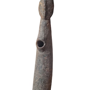 May include: A dark brown, carved wooden sculpture with a rounded head and a cylindrical body. The body features etched circular patterns and a hole. The sculpture has a weathered appearance, suggesting age and use.