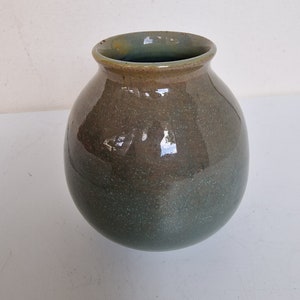 May include: A round, green ceramic vase with a brown glaze. The vase has a speckled finish and a slightly flared opening.