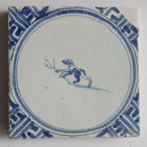 Könnte beinhalten: Eine blaue und weiße Keramikfliese mit einem stilisierten Hundedesign in der Mitte. Die Fliese hat einen blauen und weißen Rand mit einem geometrischen Muster.