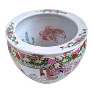 Könnte beinhalten: Eine weiße Porzellanschale mit einem breiten Rand und einem abgerundeten Boden. Die Schale ist mit einem bunten Blumenmuster verziert, darunter rosa, rote und grüne Blumen. Am Rand der Schale befindet sich ein goldener Rand. Die Schale zeigt eine Szene mit Menschen und einem Goldfisch.