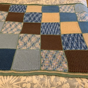 May include: A crocheted throw blanket with a patchwork design featuring squares of brown, blue and beige yarn.