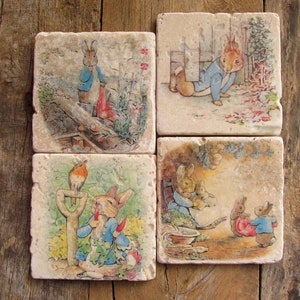 May include: Set of four square ceramic coasters featuring illustrations of Peter Rabbit from the children's book by Beatrix Potter. Each coaster depicts a different scene from the book, including Peter Rabbit in a garden, Peter Rabbit in a field, Peter Rabbit in a forest, and Peter Rabbit in a house.