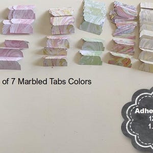 May include: Seven sets of marbled adhesive tabs in various colors including blue, pink, yellow, and green. Each set contains 12 tabs measuring 1.5 inches by 0.6 inches. The text on the image reads Choice of 7 Marbled Tabs Colors and Adhesive Tabs 12 Count 1.5 inches by 0.6 inches.