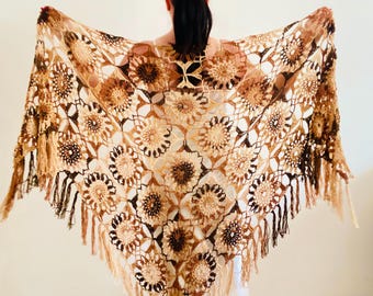 May include: A handmade, open-weave shawl in shades of brown, beige, and tan. The shawl features a floral pattern with a fringed edge. The intricate crochet design is displayed, showcasing the craftsmanship of the piece.