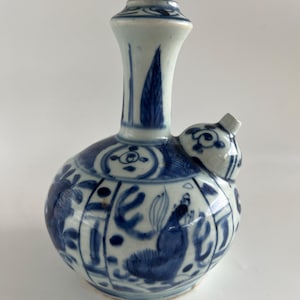 Op de afbeelding: Een blauw-witte keramische waterfles met een bolvormige body en een lange, slanke hals. De fles heeft ingewikkelde bloemen- en vogelontwerpen. De tuit is klein en schuin. Het algehele ontwerp is een klassieke, traditionele stijl.