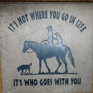 May include: A brown tile with a black silhouette of a person riding a horse with two dogs. The tile has the text "It's not where you go in life it's who goes with you".