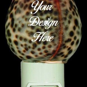 May include: A night light with a brown and white spotted seashell design. The shell has a red stripe down the center. The light has a white switch and a white base. "Your Design Here" is written on the shell.
