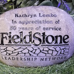 May include: A gray stone with black lettering that reads "Kathryn Lembo In appreciation of 30 years of service FieldStone LEADERSHIP NETWORK".