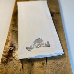 May include: White kitchen towel with a gray outline of the state of Virginia and the number 02557 printed in gray.