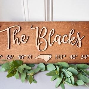 May include: A wooden sign with the text "The Blacks" in cursive script. The sign also includes the state of North Carolina and the coordinates "43° 35' 48" N 111° 42' 54" W".