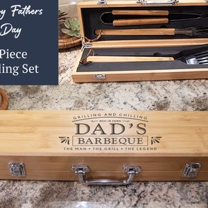 May include: A wooden box with a handle and engraved text that reads "Grilling and Chilling Best in Town Dad's Barbeque The Man The Grill The Legend". The box contains a 4-piece grilling set.