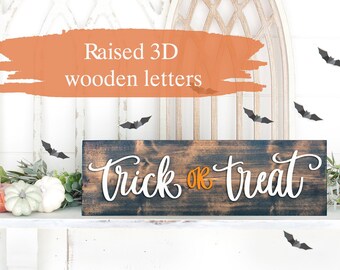 May include: A wooden sign with the words "Trick or Treat" in white raised letters. The "or" is in orange. The sign is on a white shelf with a white background.