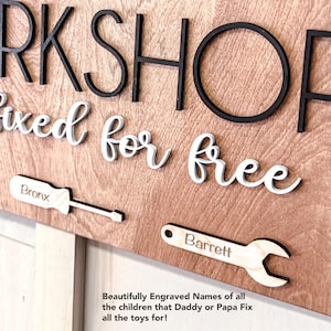 May include: Wooden sign with the words "Workshop" and "Fixed for free" in black and white lettering. The sign also features two tools, a screwdriver and a wrench, with the names "Bronx" and "Barrett" engraved on them.