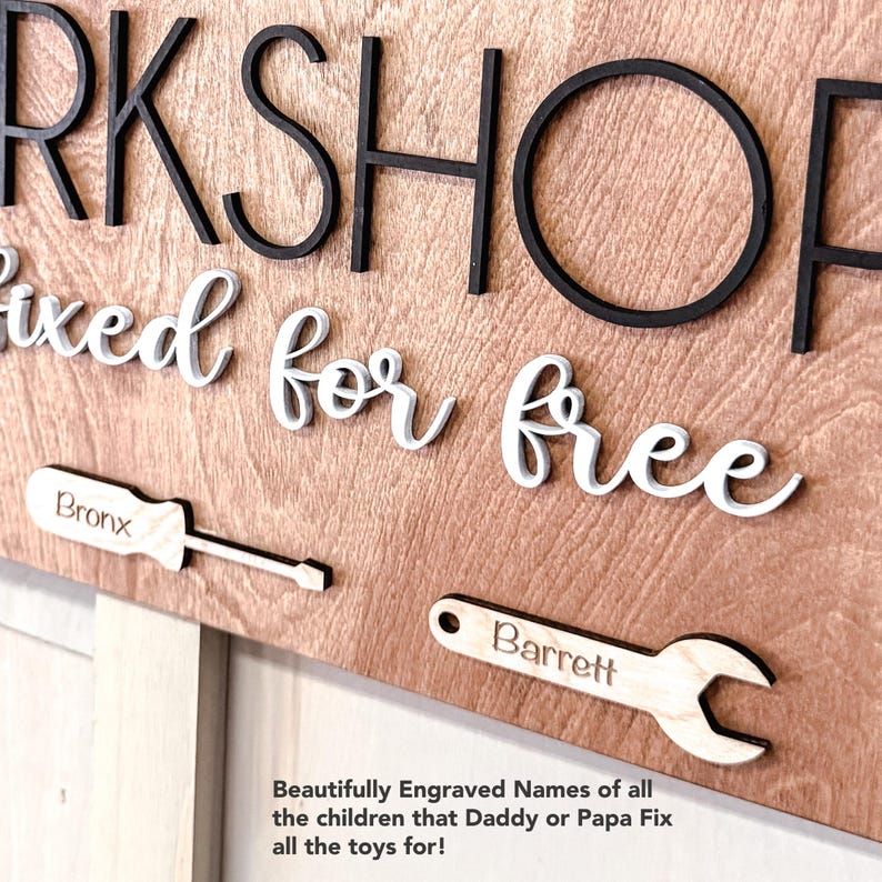 May include: Wooden sign with the words "Workshop" and "Fixed for free" in black and white lettering. The sign also features two tools, a screwdriver and a wrench, with the names "Bronx" and "Barrett" engraved on them.