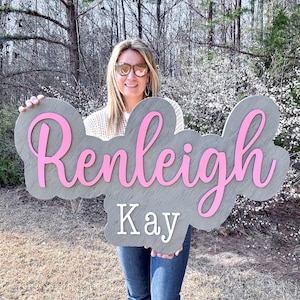 May include: A gray wooden sign with the name "Renleigh Kay" written in pink cursive letters.