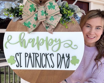May include: A round wooden door hanger with a green and brown burlap bow and green shamrock accents. The sign reads "Happy St. Patrick's Day".